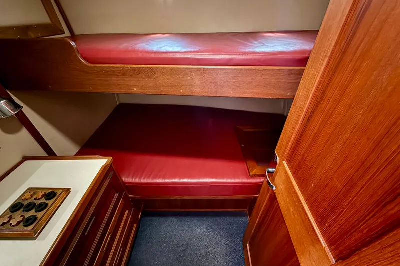 Slide: The Image of Interior of a 2000 Nordic Tug 37 featuring red cushioned bunk beds and wooden cabinetry. - 54