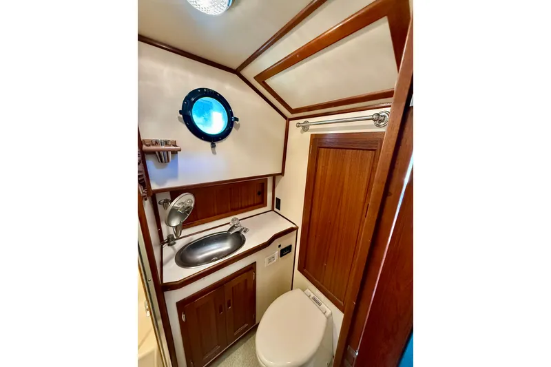 Slide: The Image of Compact bathroom in a 2000 Nordic Tug 37, featuring wood accents and a porthole window. - 52