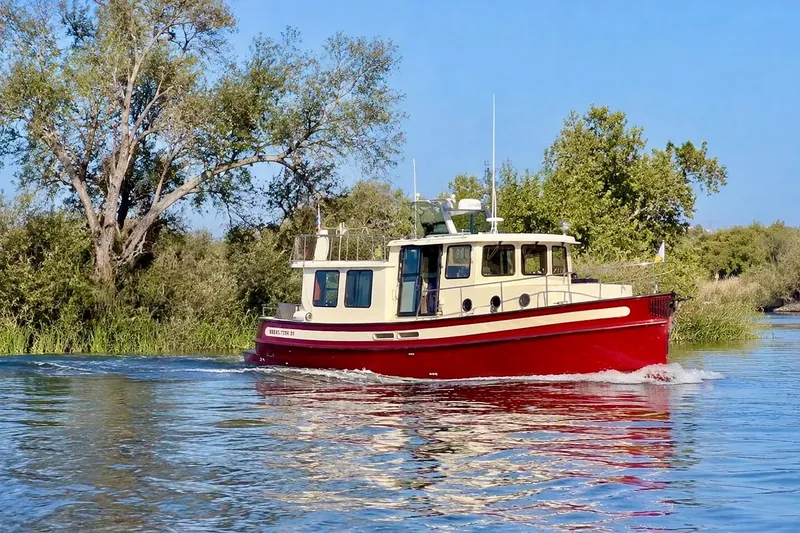 Slide: The Image of A 2000 Nordic Tug 37 cruising on a serene river with lush greenery. - 3
