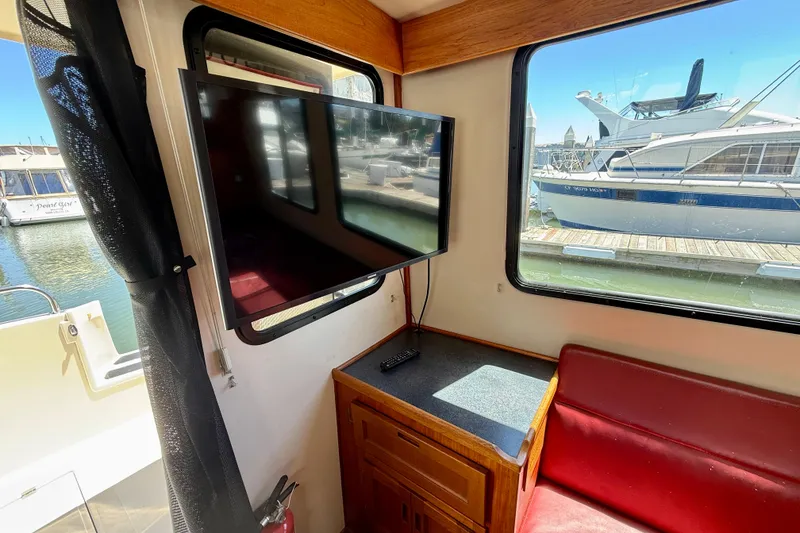 Slide: The Image of Interior of a 2000 Nordic Tug 37 with TV, red seating, and marina view. - 72