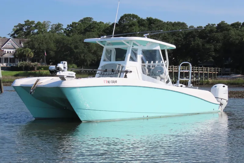 Slide: The Image of 2023 Twin Vee 260 GFX CC catamaran in calm waters, surrounded by lush greenery. - 12