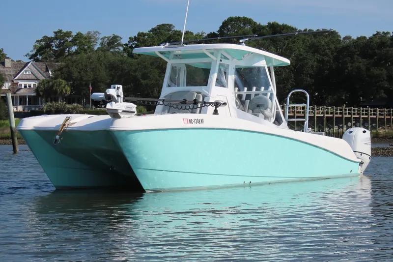 Slide: The Image of 2023 Twin Vee 260 GFX CC catamaran in calm waters, with a scenic background. - 7