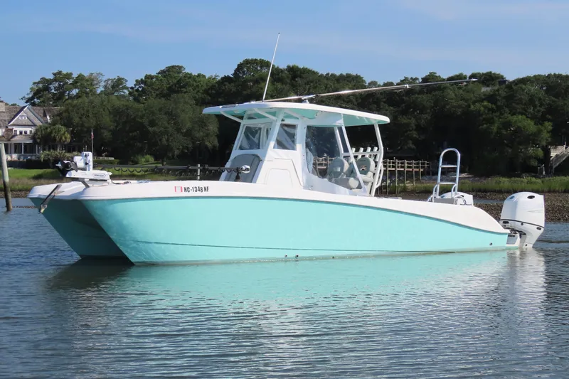 Slide: The Image of 2023 Twin Vee 260 GFX CC boat on calm water, surrounded by lush greenery. - 10