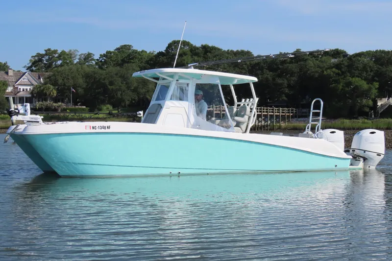 Slide: The Image of 2023 Twin Vee 260 GFX CC boat on calm water, surrounded by lush greenery. - 2
