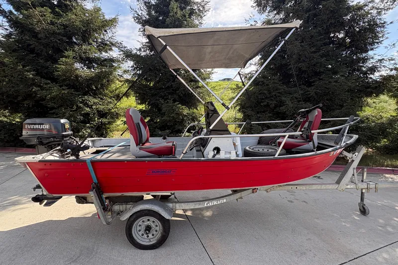 Slide: The Image of 1997 Duroboat 14rlw with Evinrude motor on trailer, red color, outdoor setting. - 2