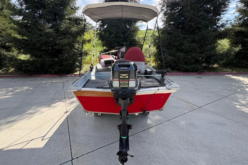 Slide: The Image of 1997 Duroboat 14rlw with outboard motor, parked on concrete, surrounded by trees. - 7