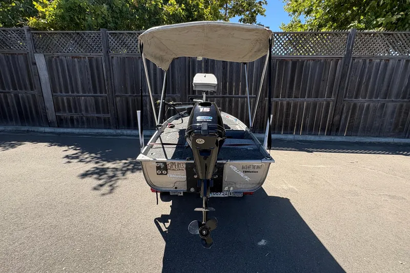 Slide: The Image of 1994 Grumman 1065 boat with motor, parked on pavement, wooden fence background. - 21