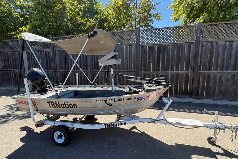 Slide: The Image of 1994 Grumman 1065 boat on trailer with canopy, parked by wooden fence. - 6