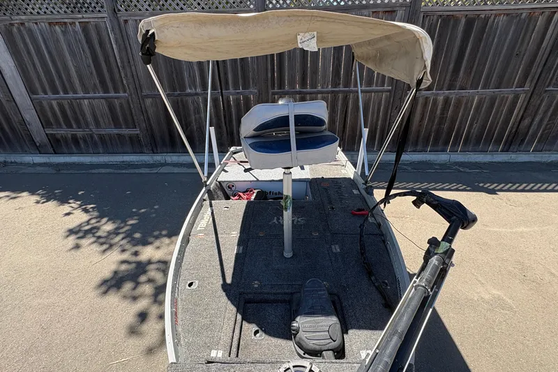 Slide: The Image of 1994 Grumman 1065 boat with canopy and seating, parked by a wooden fence. - 9