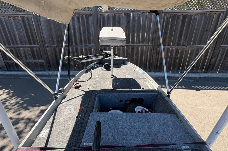 Slide: The Image of 1994 Grumman 1065 boat interior with canopy and equipment, parked by a wooden fence. - 22