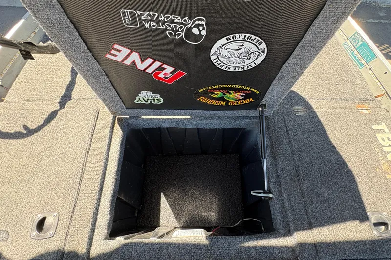 Slide: The Image of Open storage compartment in a 1994 Grumman 1065 boat, featuring various stickers. - 20