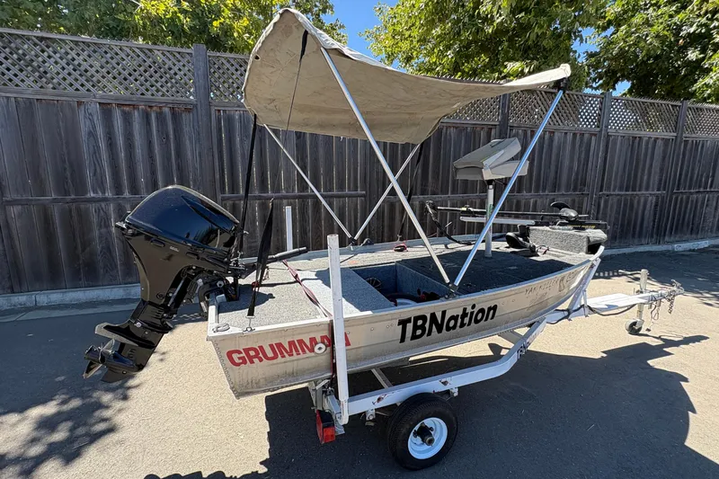 Slide: The Image of 1994 Grumman 1065 boat with canopy and motor on trailer, parked outdoors. - 5