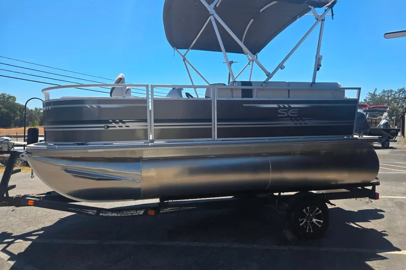 Slide: The Image of 2025 BERSHIRE SE 16 pontoon boat on trailer, parked outdoors under clear sky. - 2