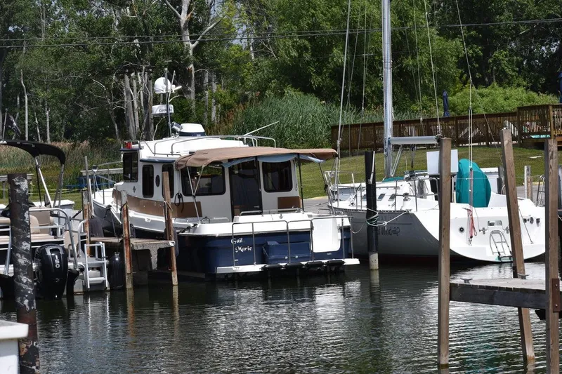 Slide: The Image of 2013 Ranger Tugs R-29 docked at a marina, surrounded by lush greenery. - 16