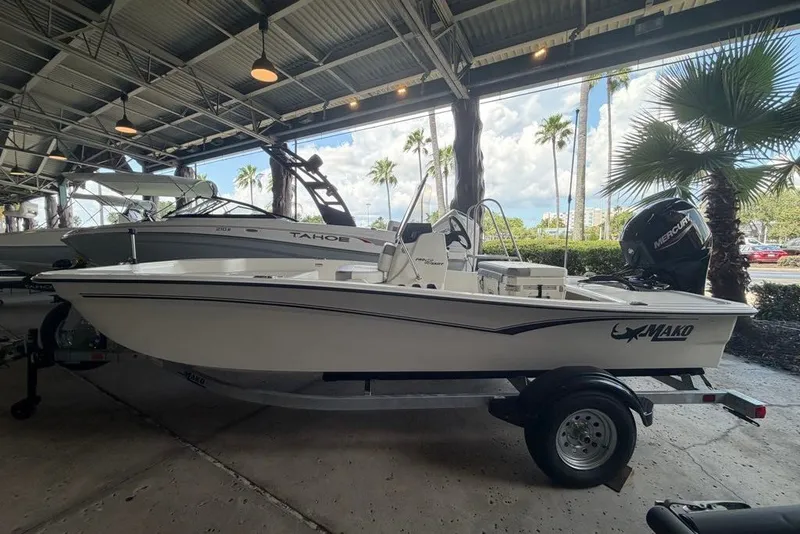 The Image of 2026 Mako Pro Skiff 15 CC boat displayed in a covered showroom with palm trees outside. - 0