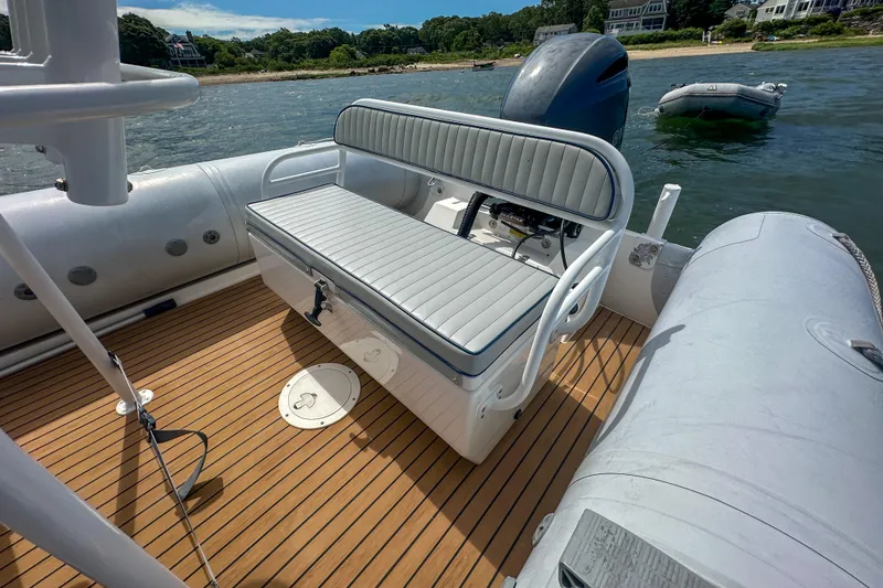 Slide: The Image of 2019 Ribcraft 6.8 boat interior with cushioned seating and wooden deck, near shoreline. - 20