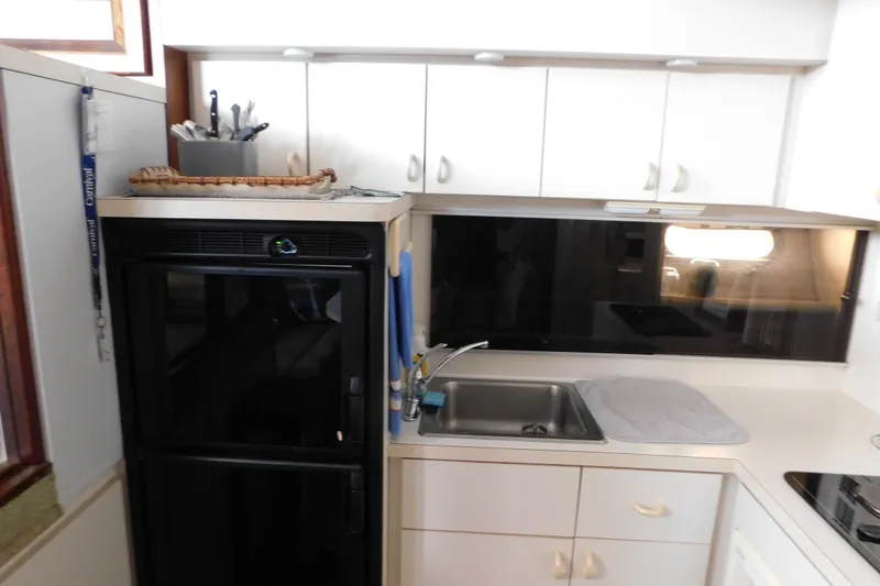 Slide: The Image of 1992 Silverton 41 Aft Cabin kitchen with sink, black fridge, and white cabinets. - 63