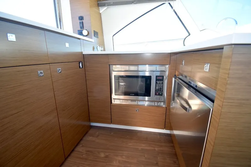 Slide: The Image of The 2019 Cruisers Yachts 50 Cantius kitchen features modern wood cabinets, a microwave, and a dishwasher. - 11