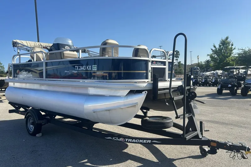 The Image of 2023 Sun Tracker Bass Buggy 16 XL Select pontoon boat on trailer in parking lot. - 1