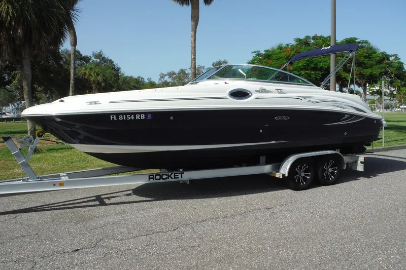 The Image of 2005 Sea Ray 240 Sundeck boat on trailer, parked outdoors with trees in background. - 0