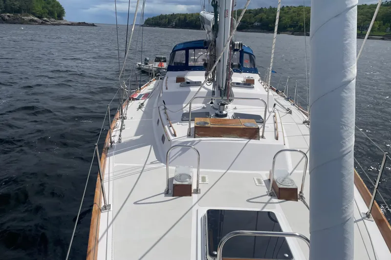 Slide: The Image of Hinckley Sou'wester 59 sailboat deck view, 1985 model, on calm waters near a forested shoreline. - 6