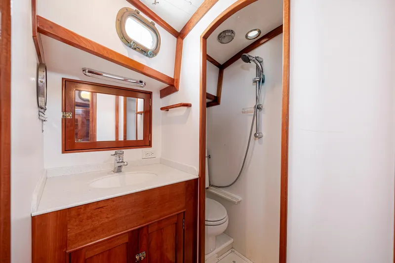 Slide: The Image of Compact boat bathroom with wooden accents, featuring a sink, mirror, and shower in a 2001 Shannon 47/52. - 62