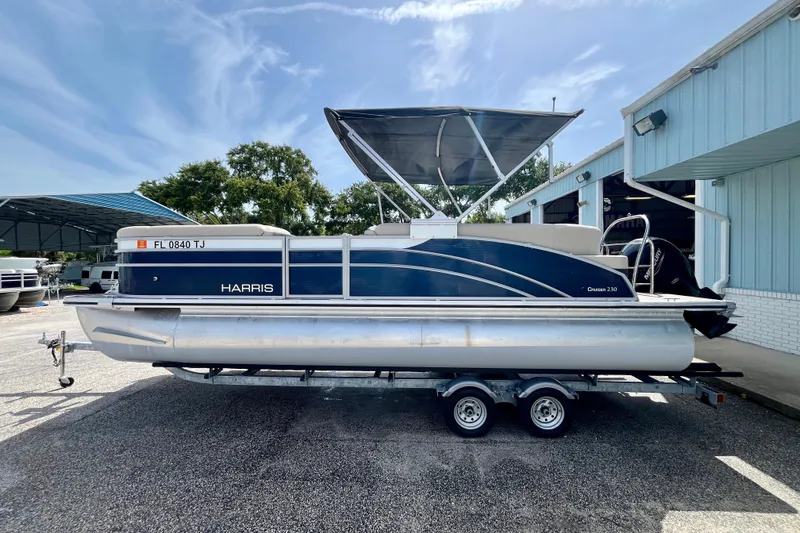 The Image of 2023 Harris Cruiser 230 pontoon boat on trailer, parked outdoors under clear sky. - 1