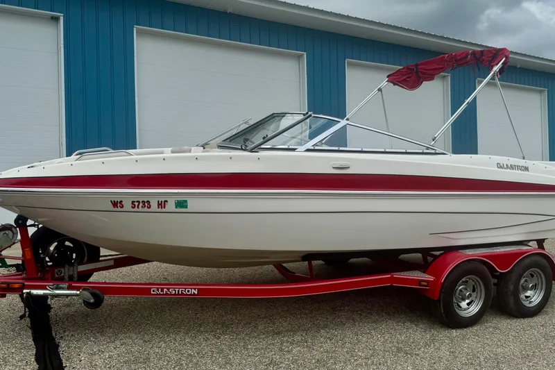 Slide: The Image of 2008 Glastron GT 225 boat on red trailer, parked near blue building. - 1