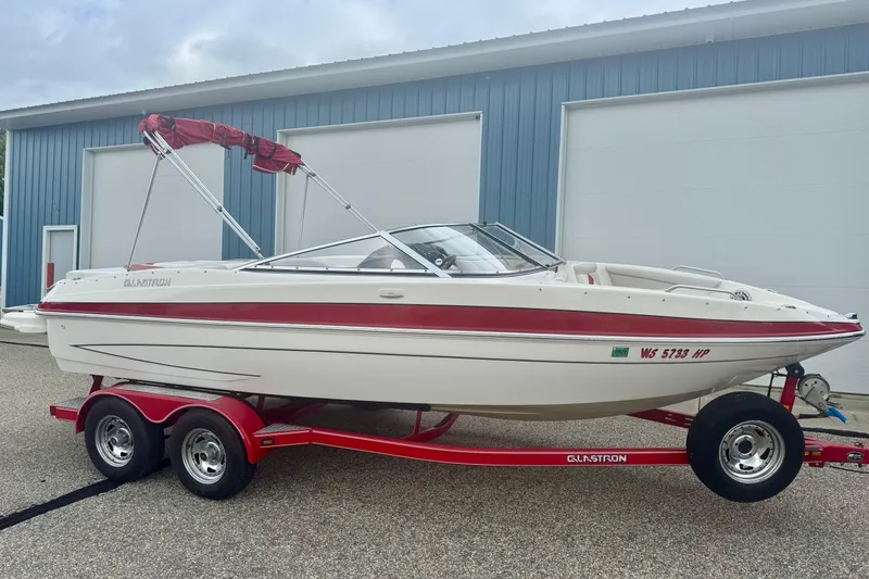 Slide: The Image of 2008 Glastron GT 225 boat on red trailer, parked outside blue building. - 2