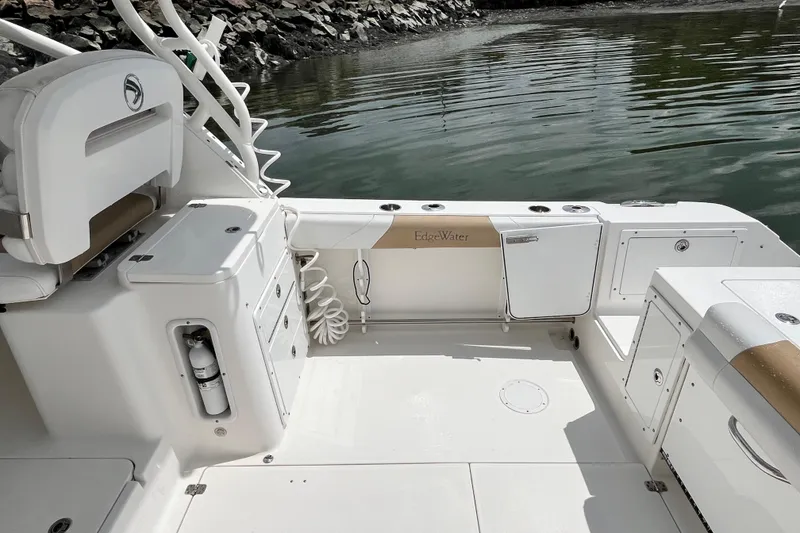 Slide: The Image of 2014 Edgewater 280CX Crossover boat interior, featuring seating and storage, docked by rocky shoreline. - 15