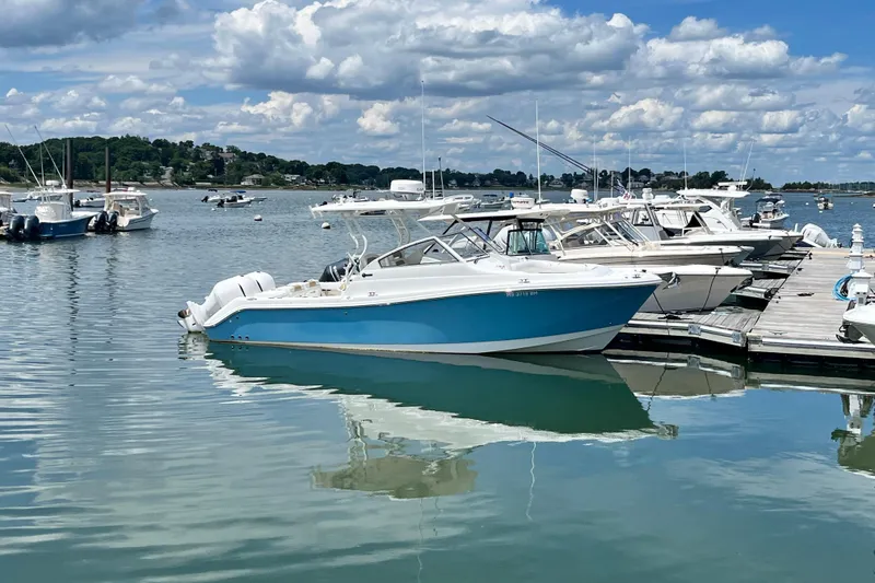 Slide: The Image of 2014 Edgewater 280CX Crossover boat docked in a serene marina under a cloudy sky. - 1
