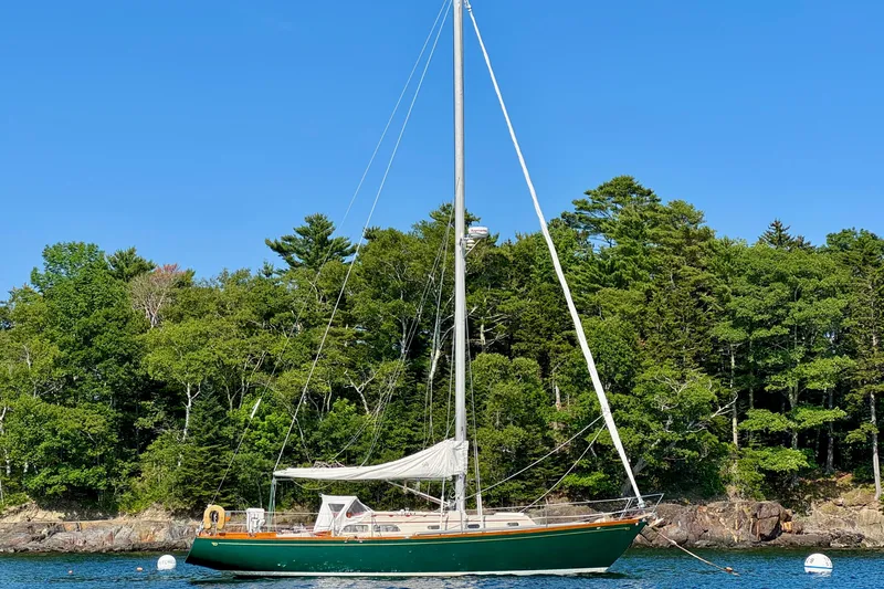 Slide: The Image of Vintage 1970 Hincley 38 sailboat anchored near lush green forest and clear blue sky. - 2