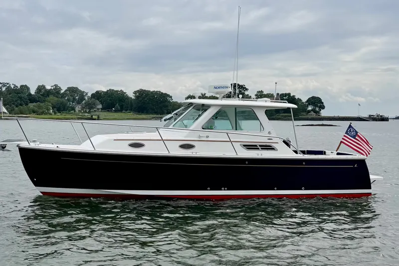 The Image of 2006 Back Cove 29 boat on water, American flag, overcast sky, shoreline in background. - 0
