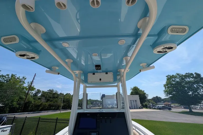 Slide: The Image of 2020 NauticStar 2602 Legacy boat with blue T-top and rod holders, parked outdoors. - 6