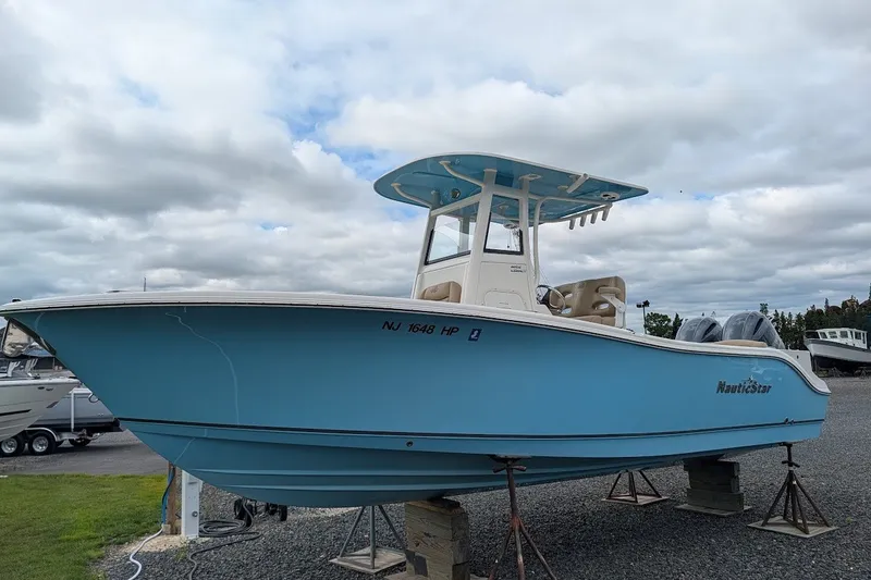 The Image of 2020 NauticStar 2602 Legacy boat on stands, blue hull, cloudy sky background. - 0