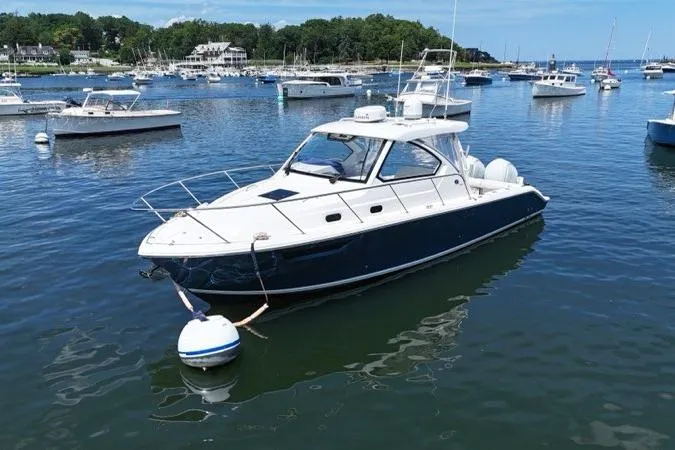 Slide: The Image of 2022 Pursuit OS 325 Offshore boat moored in a scenic harbor with other vessels. - 2