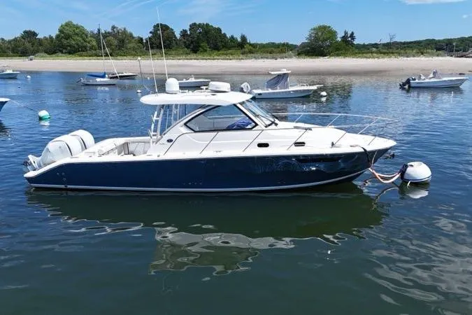The Image of 2022 Pursuit OS 325 Offshore boat anchored in calm waters near a sandy shoreline. - 0