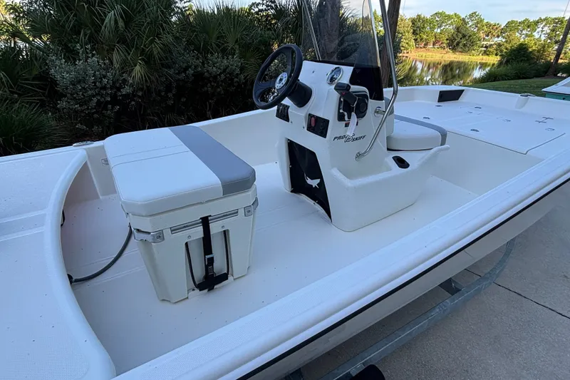 Slide: The Image of 2026 Mako Pro Skiff 15 CC boat interior with console and seating, near a scenic lake. - 4