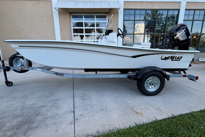 Slide: The Image of 2026 Mako Pro Skiff 15 CC boat on trailer, parked outside a building. - 1