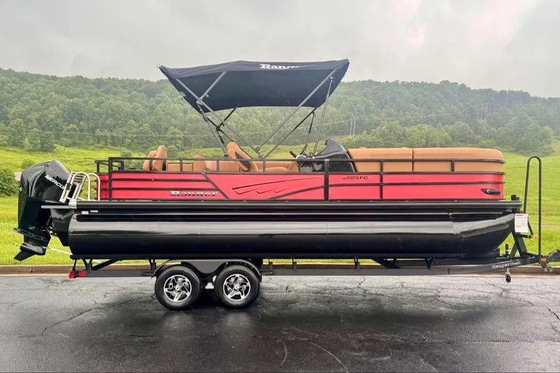 The Image of 2026 Ranger 223FC pontoon boat with canopy, parked on trailer, scenic background. - 0
