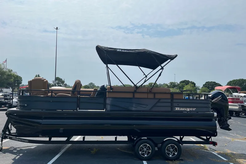 Slide: The Image of 2026 Ranger 220FC pontoon boat with canopy, parked on a trailer in a lot. - 2