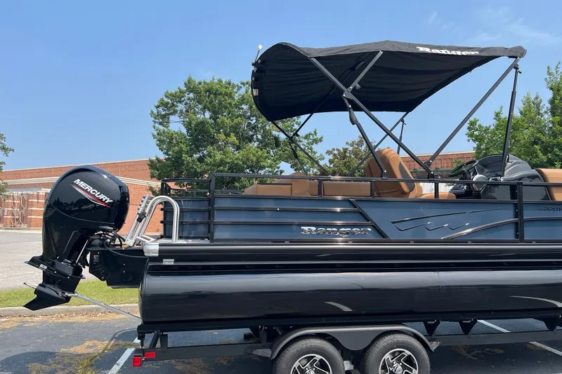 Slide: The Image of 2026 Ranger 220FC pontoon boat with Mercury outboard motor, parked on a trailer. - 3