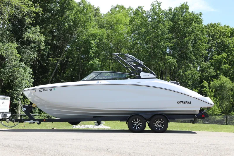 Slide: The Image of 2023 Yamaha Boats 252S on trailer, parked outdoors with lush green trees in background. - 6