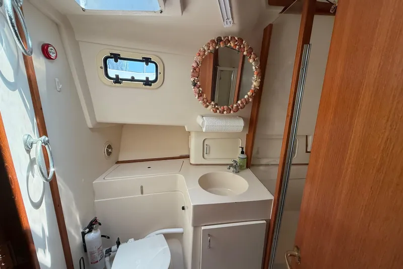 Slide: The Image of Bathroom interior of 2000 Mainship 390 Trawler with sink, mirror, and porthole window. - 74