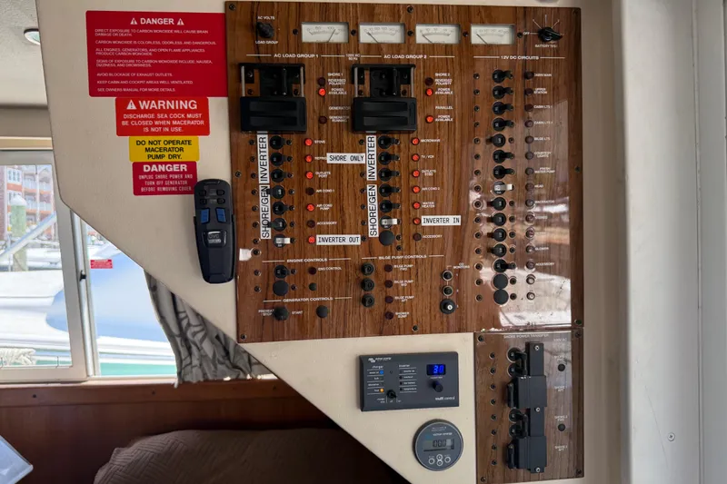 Slide: The Image of Control panel of a 2000 Mainship 390 Trawler with various switches and warning labels. - 77