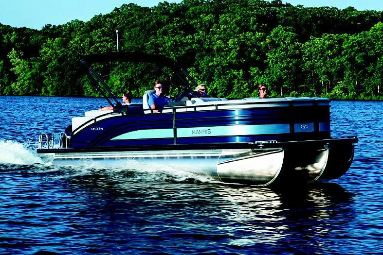Slide: The Image of Manufacturer Provided Image: 2021 Harris Solstice 230 pontoon boat cruising on a lake with lush green trees in the background. - 2