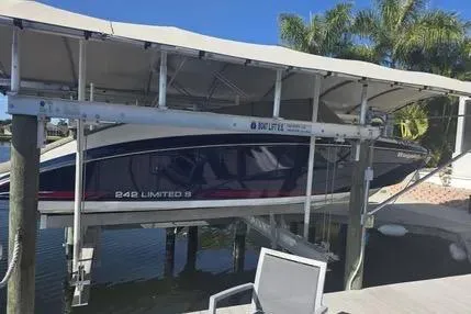 Slide: The Image of 2016 Yamaha Boats 242 Limited S E-Series on lift, dockside with palm trees in background. - 2