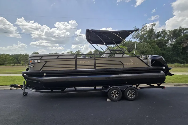 Slide: The Image of 2019 Regency 230 LE3 Sport pontoon boat on trailer, parked outdoors under a cloudy sky. - 4