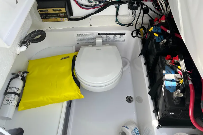 Slide: The Image of 2024 Sportsman Heritage 231 Center Console boat interior with toilet, batteries, and safety equipment. - 14