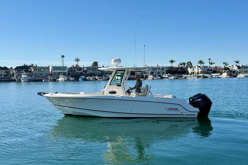 Slide: The Image of 2025 Boston Whaler 250 Outrage boat cruising on calm water near a marina. - 6